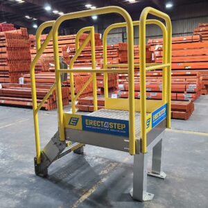 A bright yellow ErectaStep platform ladder is positioned in a well-organized warehouse. The ladder features a sturdy, slip-resistant platform with safety guardrails surrounding it. The ErectaStep branding, along with the company's website and contact number, is prominently displayed on the side of the platform. The ladder is securely bolted to a solid, gray base for stability. In the background, stacks of orange metal beams and other industrial components are neatly arranged, indicating a highly organized storage system within the warehouse environment.